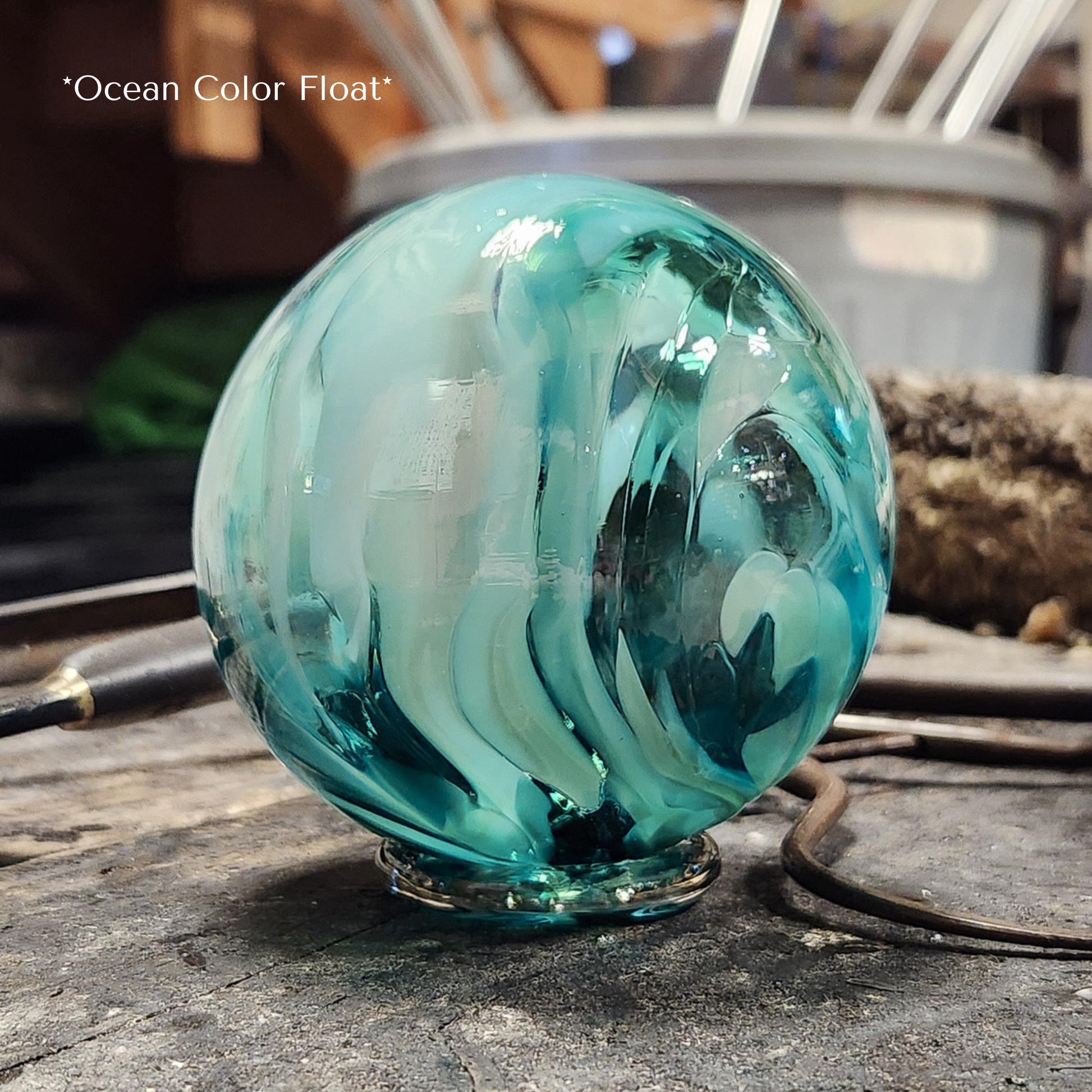 multiple shades of teal blown glass float sitting on the artists work bench with tools around