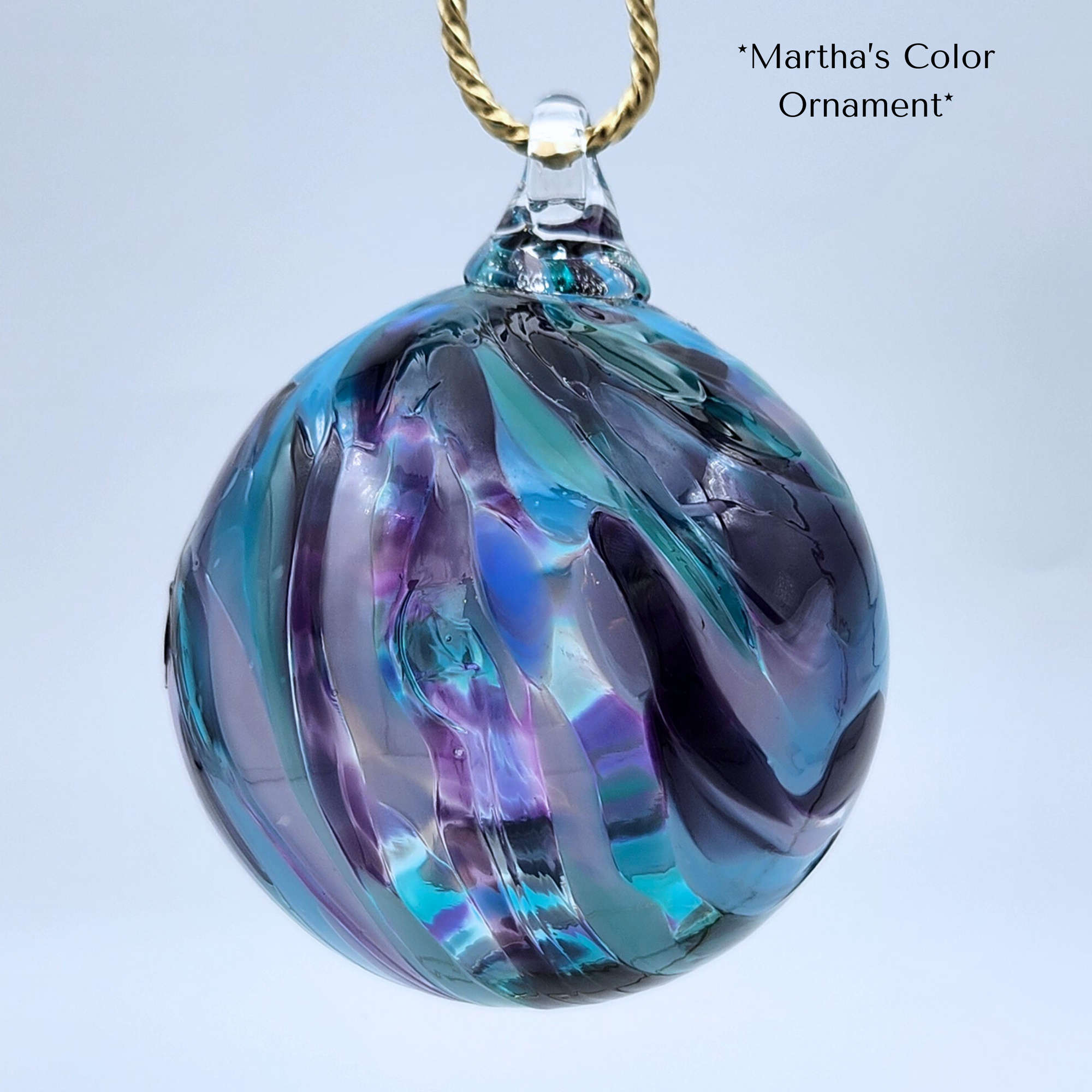 Glass ornament with purple and blue swirls on a gold chain against a light gray background.
