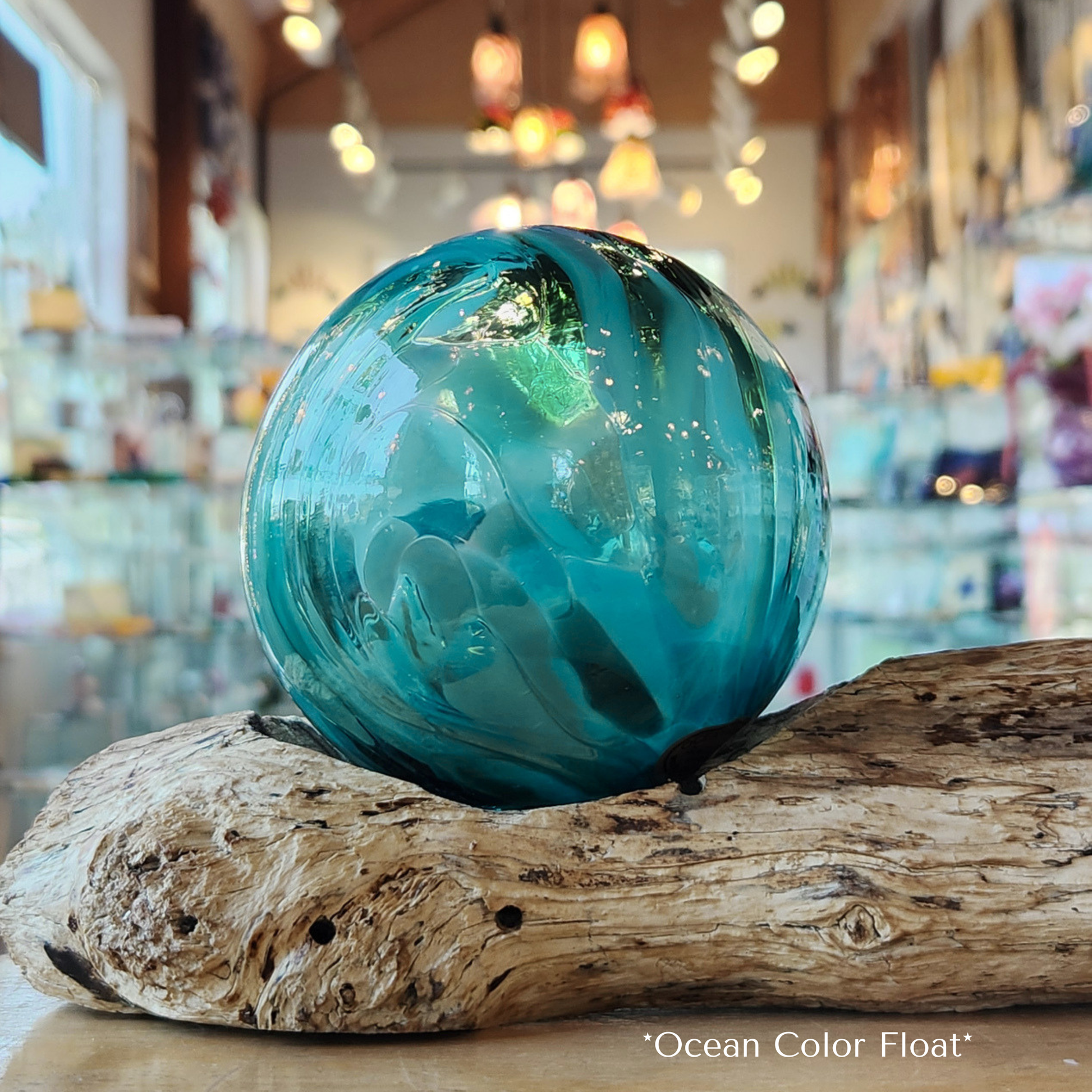 Multiple shades of teal glass float sitting on driftwood with a gallery setting in the background